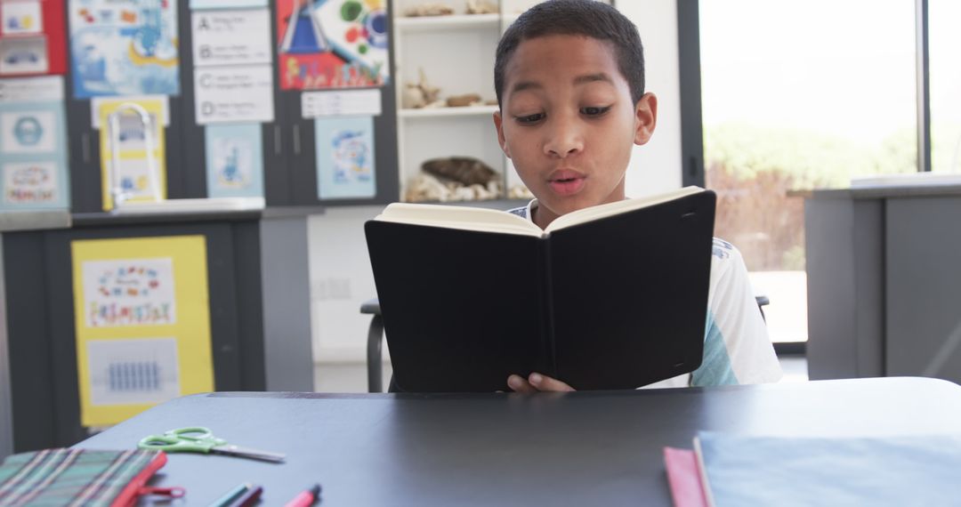 Young Student Reading Book in Classroom Surrounded by Learning Materials