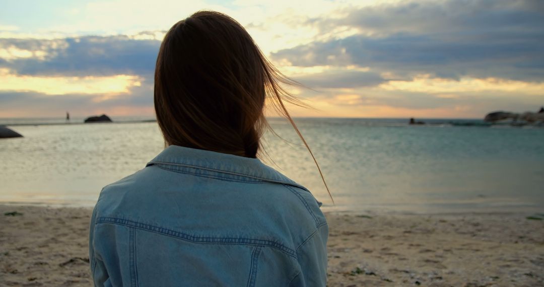 Back view of caucasian woman standing and looking at sea on beach at sundown - Free Images, Stock Photos and Pictures on Pikwizard.com