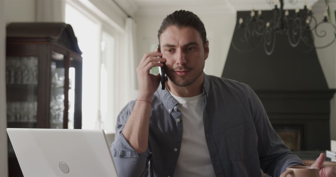 Man Multitasking with Smartphone and Laptop in Home Office