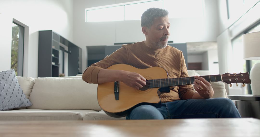 Man playing guitar on couch in modern living room - Free Images, Stock Photos and Pictures on Pikwizard.com