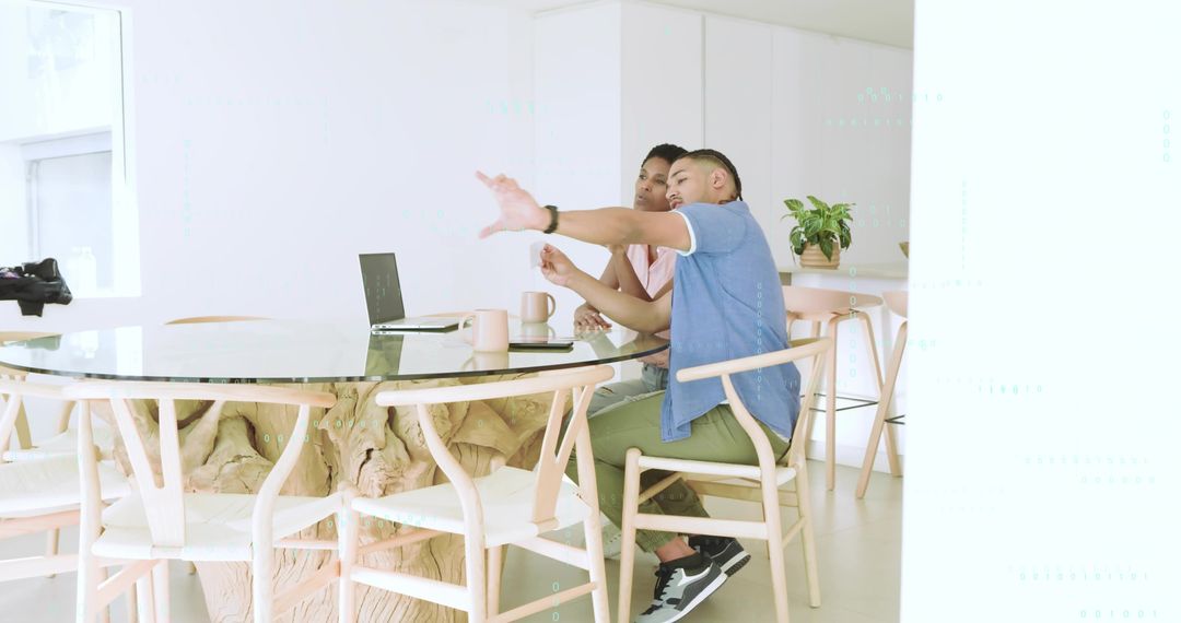 Man pointing while woman watching at glass-top kitchen table with laptop