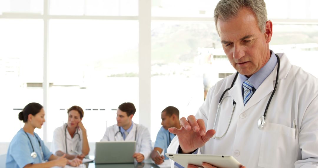 Male Doctor Using Digital Tablet with Medical Team Meeting in Background - Free Images, Stock Photos and Pictures on Pikwizard.com