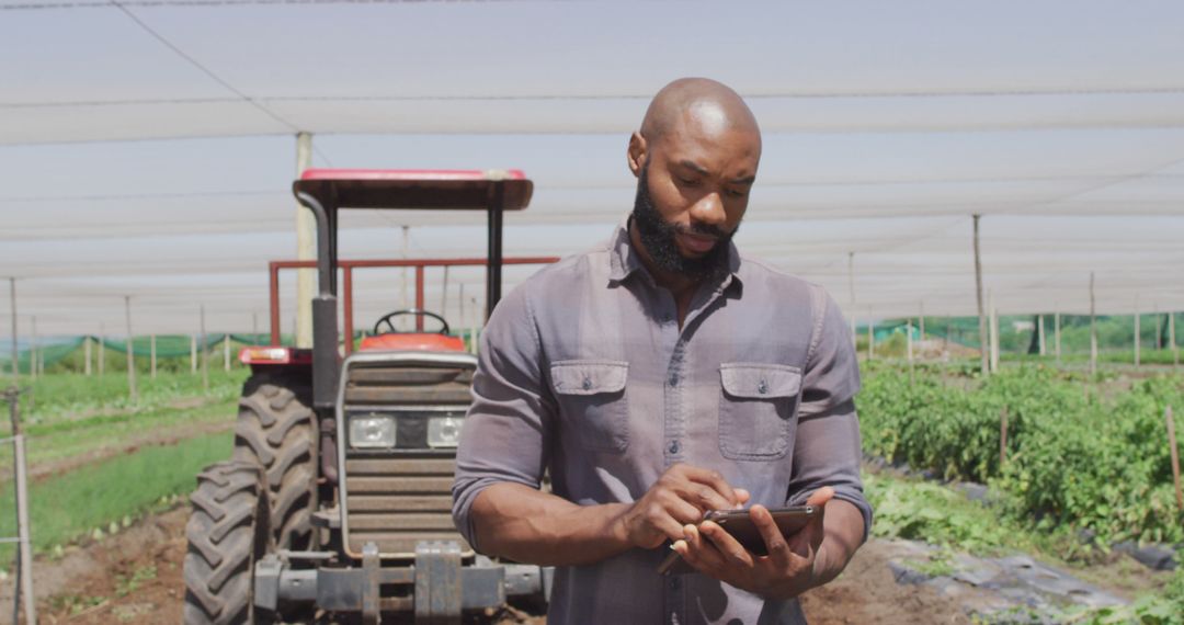 African American farmer using digital tablet in field with tractor - Free Images, Stock Photos and Pictures on Pikwizard.com