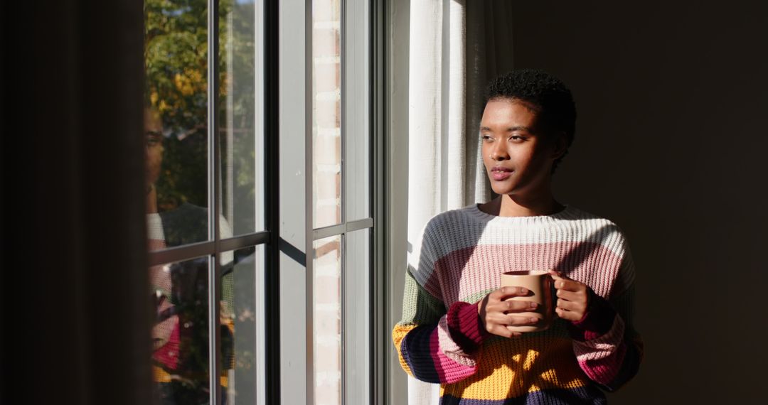 Woman in Colorful Sweater Holding Mug and Gazing Through Window