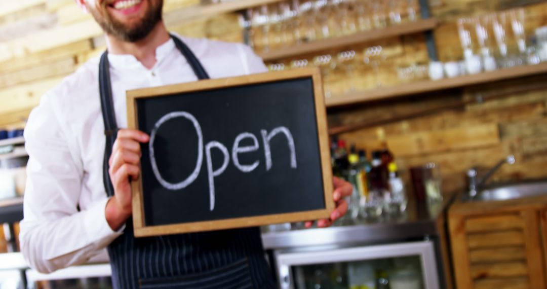 Smiling waiter holding an open sign in a cozy cafe - Free Images, Stock Photos and Pictures on Pikwizard.com