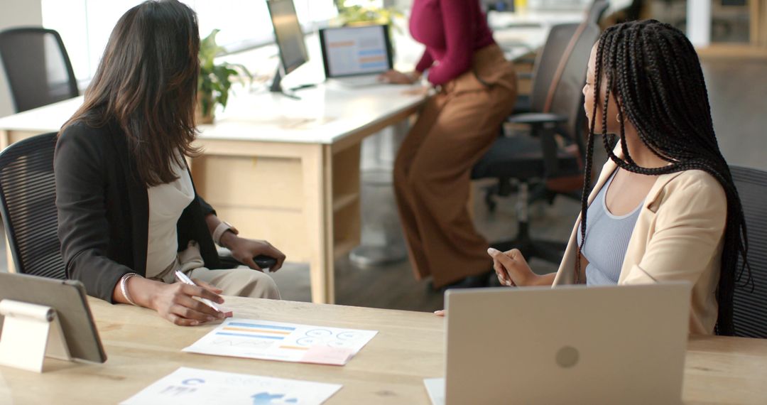Diverse female team collaborating over analytics charts and laptops in modern office