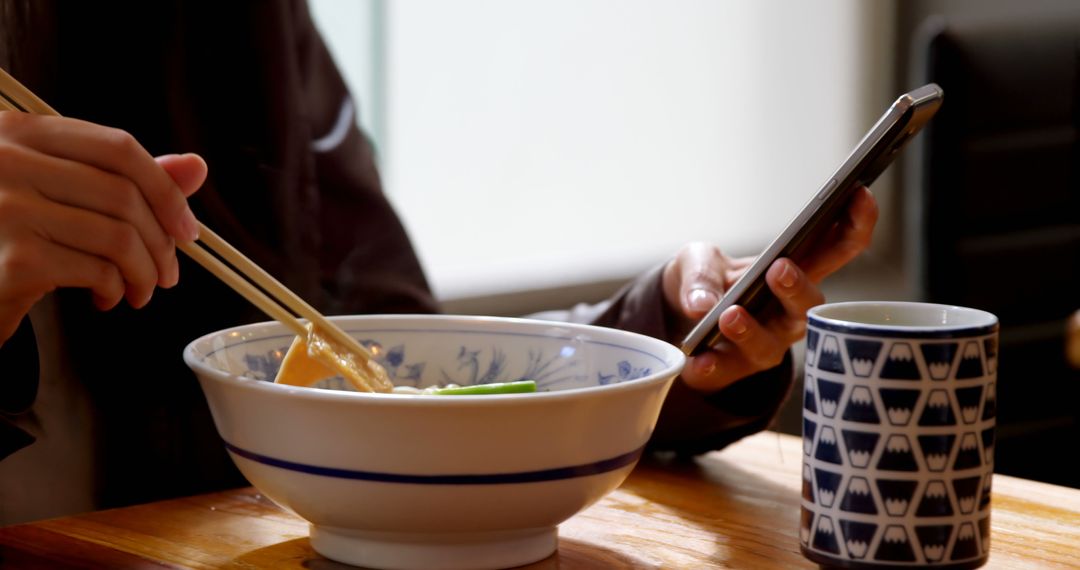 Person Eating Noodles Using Smartphone at Table - Free Images, Stock Photos and Pictures on Pikwizard.com