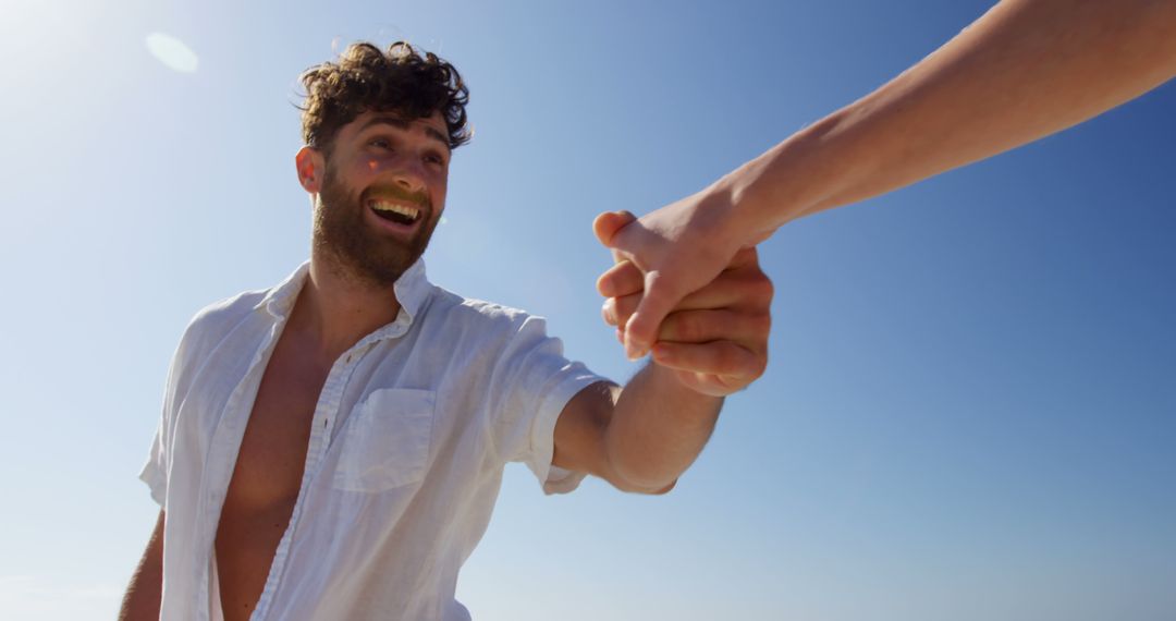 Happy man holding hand of friend on sunny beach day - Free Images, Stock Photos and Pictures on Pikwizard.com