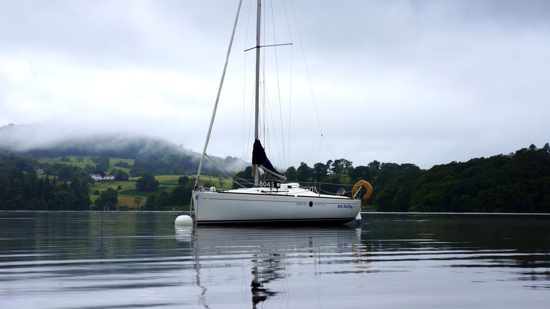 Sailboat Anchored in Tranquil Lake with Misty Hills in Background - Free Images, Stock Photos and Pictures on Pikwizard.com