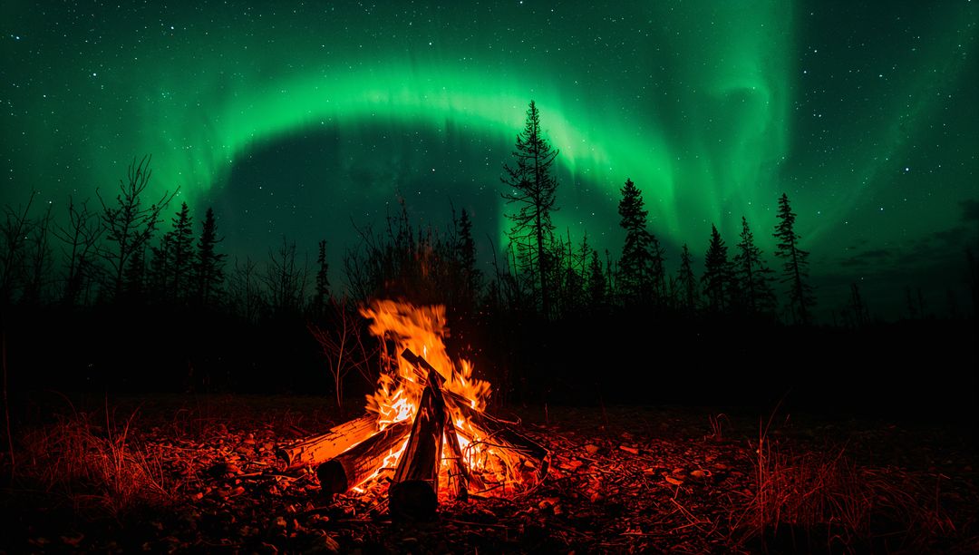 Glowing Campfire Under Dancing Aurora Borealis Over Pine Forest Night Sky