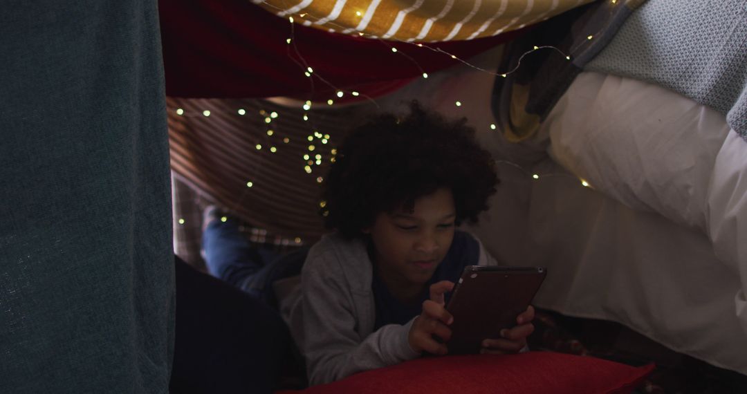 Young Boy Playing on Tablet in Cozy Blanket Fort Illuminated by String Lights - Free Images, Stock Photos and Pictures on Pikwizard.com