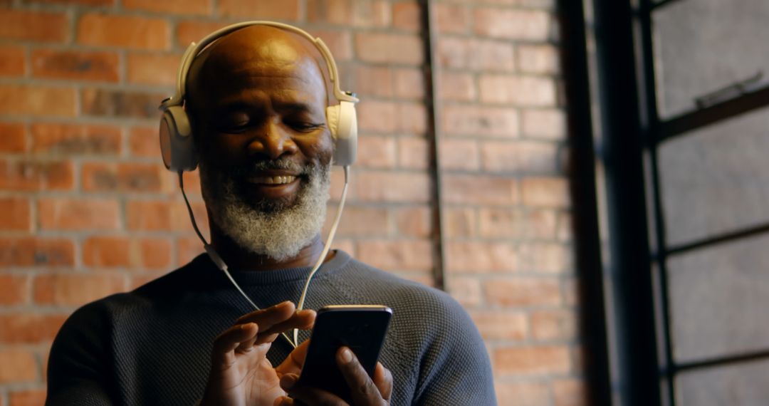 Senior Man Smiling and Listening to Music on Phone with Headphones - Free Images, Stock Photos and Pictures on Pikwizard.com