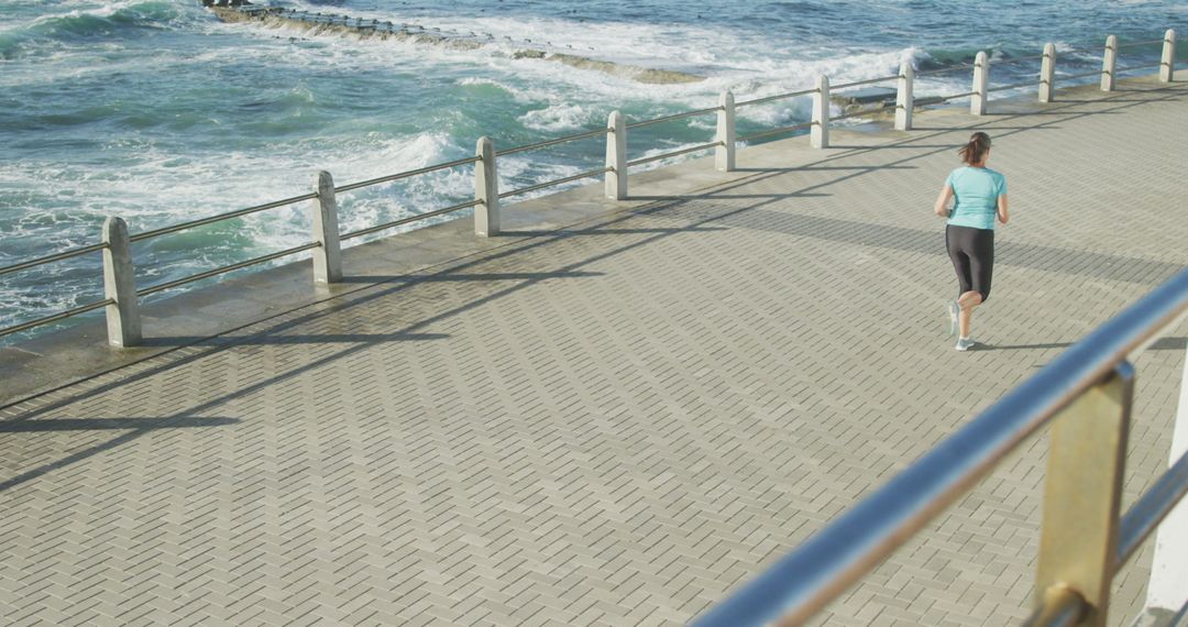 Woman Jogging Along Oceanfront Boardwalk on a Sunny Day - Free Images, Stock Photos and Pictures on Pikwizard.com