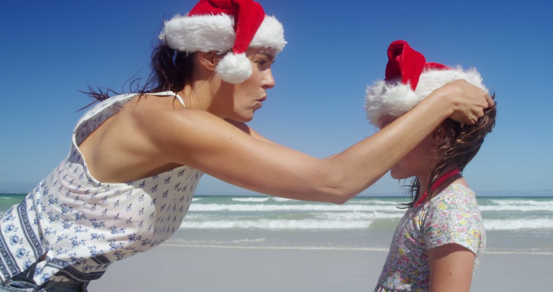 Mother Adjusting Daughter's Santa Hat on Sunny Beach - Free Images, Stock Photos and Pictures on Pikwizard.com