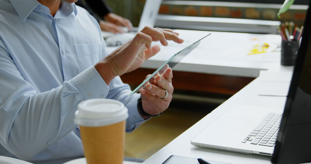 Businessman Using Tablet at Office Desk with Laptop and Coffee - Free Images, Stock Photos and Pictures on Pikwizard.com