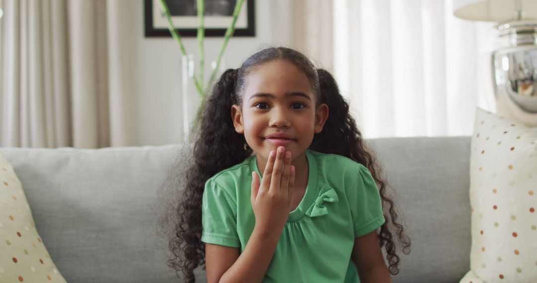 Happy biracial girl sitting on sofa using sign language - Free Images, Stock Photos and Pictures on Pikwizard.com