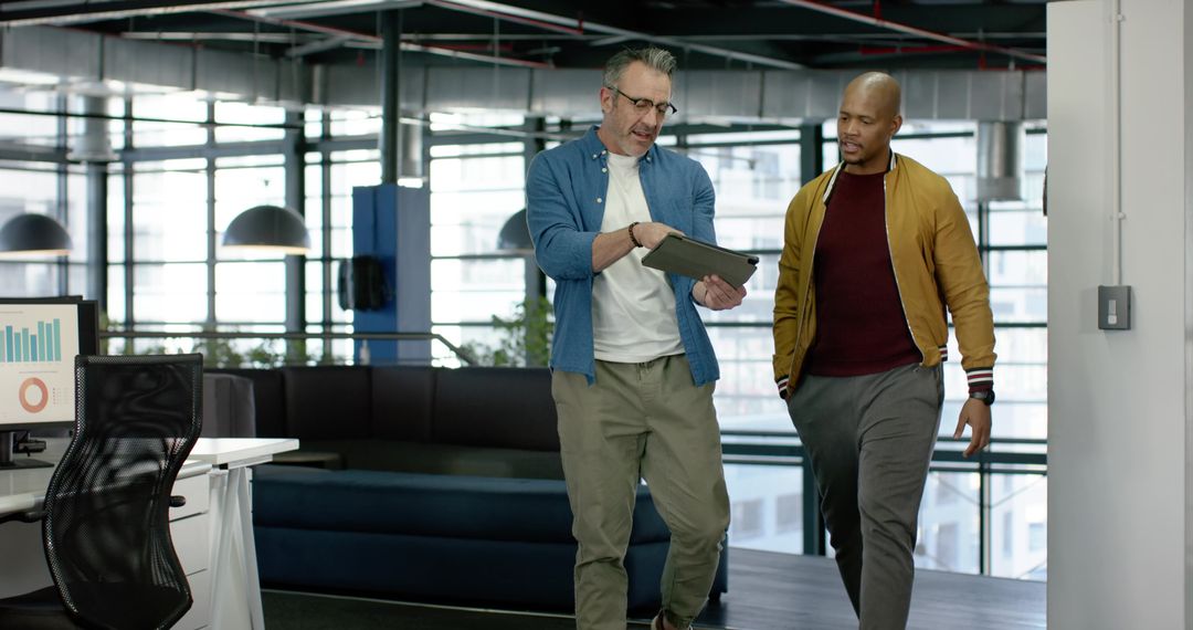 Diverse colleagues walking and discussing tablet in modern mezzanine office