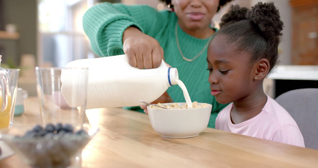 Mother Pouring Milk into Daughter's Cereal Bowl at Breakfast Table - Free Images, Stock Photos and Pictures on Pikwizard.com