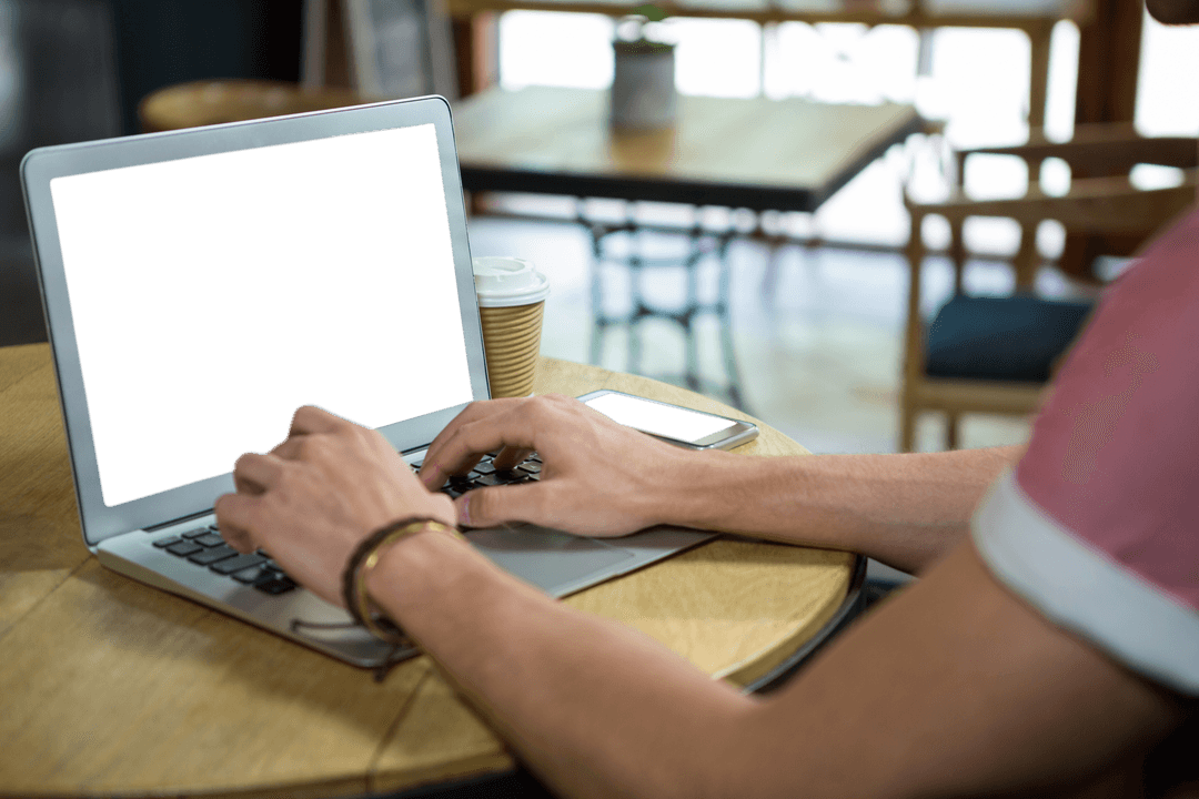 Male Hands Typing on Laptop with Blank Screen in Cozy Cafe Environment