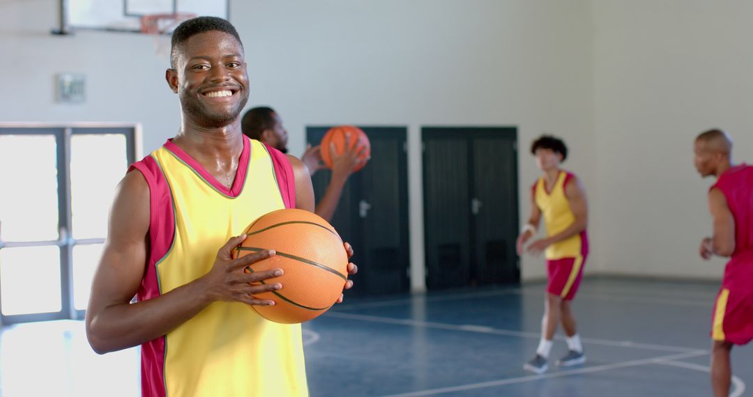 Smiling Athlete Holding Basketball in Gym with Teammates Practicing