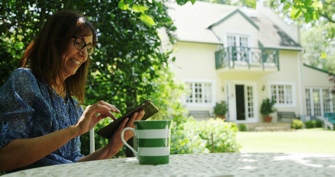 Older Lady Enjoying Tablet in Garden by House - Free Images, Stock Photos and Pictures on Pikwizard.com