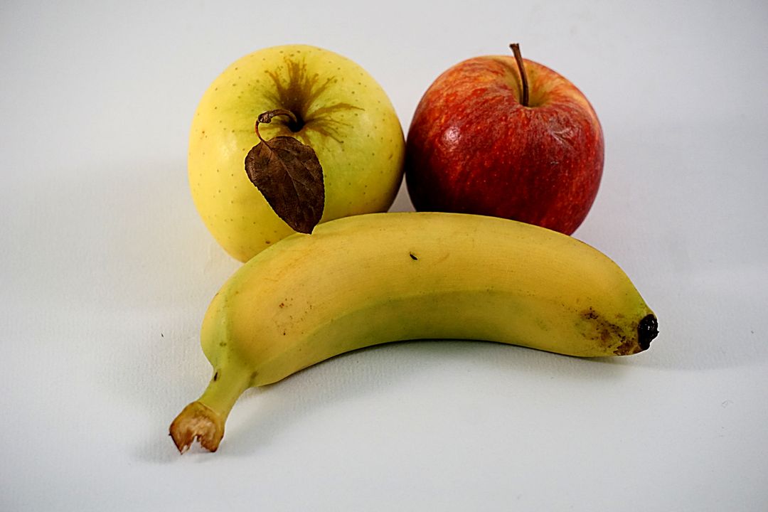 Banana and two apples resting on white background for healthy snack concept