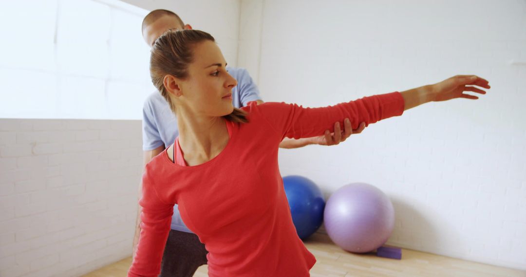 Female client stretching with trainer in rehab studio using stability balls for mobility