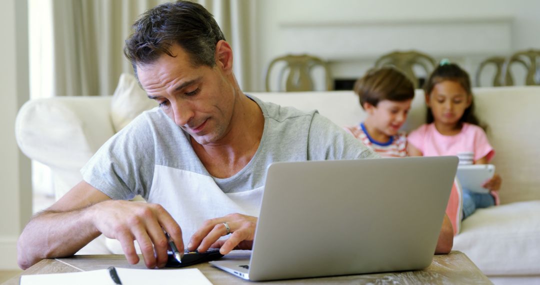 Focused Father Working from Home with Children Playing in Background - Free Images, Stock Photos and Pictures on Pikwizard.com