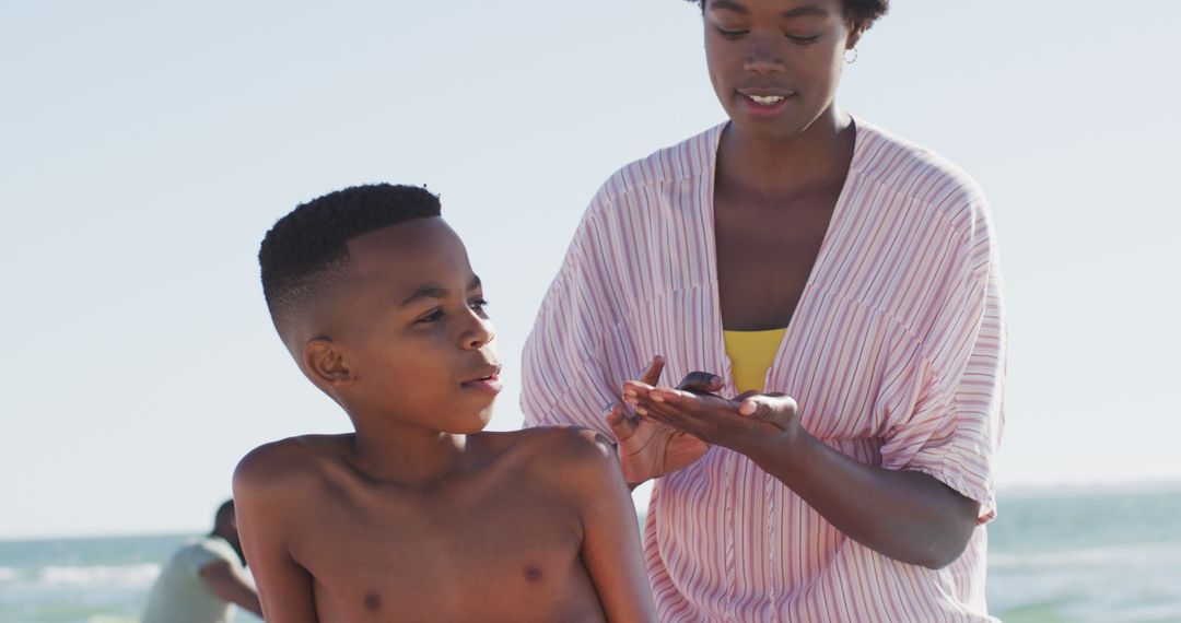 Mother applying sunscreen to son on beach - Free Images, Stock Photos and Pictures on Pikwizard.com