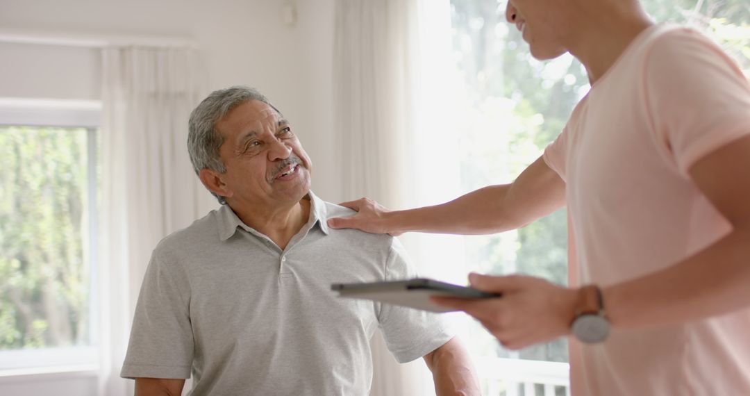 Elderly man smiling while talking with caregiver at home - Free Images, Stock Photos and Pictures on Pikwizard.com