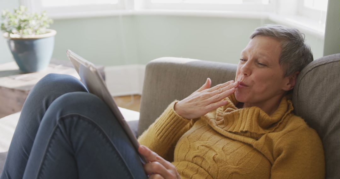 Elderly Woman Using Tablet and Sending Air Kiss on Sofa - Free Images, Stock Photos and Pictures on Pikwizard.com