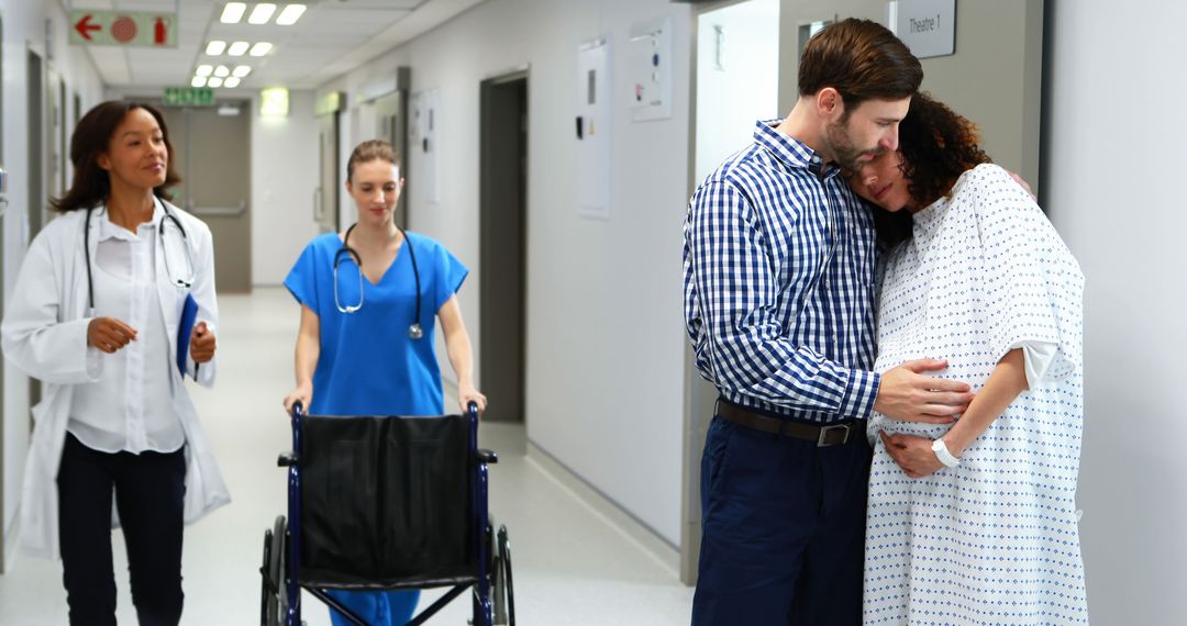 Pregnant Woman and Partner Embracing in Hospital Corridor, Medical Staff Assisting - Free Images, Stock Photos and Pictures on Pikwizard.com