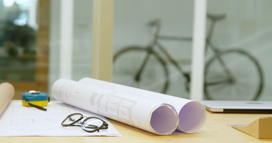 Architectural plans on desk with bicycle in background - Free Images, Stock Photos and Pictures on Pikwizard.com