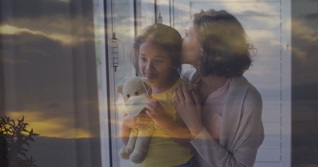 Mother Embracing Daughter by Window With Teddy Bear