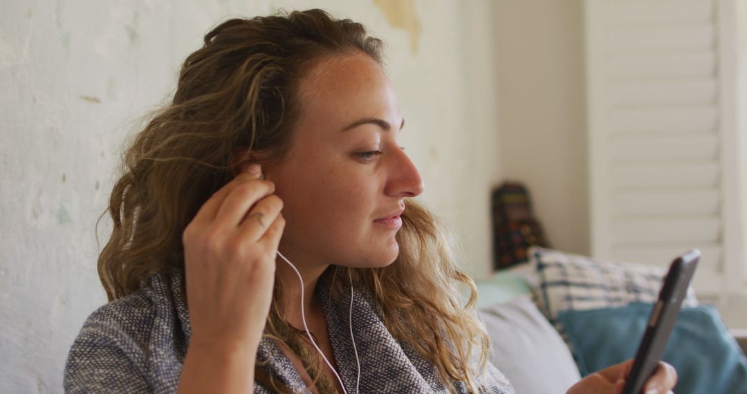 Young Woman Using Smartphone Earbuds Focused Look Relaxing at Home - Free Images, Stock Photos and Pictures on Pikwizard.com