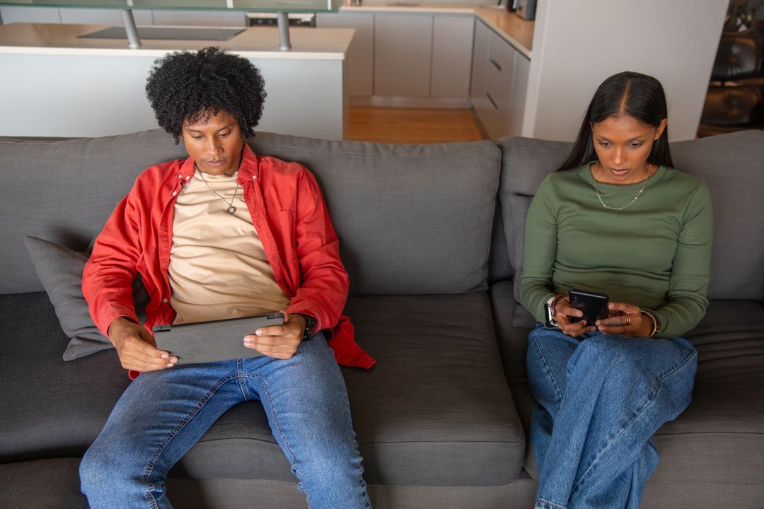 Diverse Couple Browsing Devices on Sofa in Modern Living Room