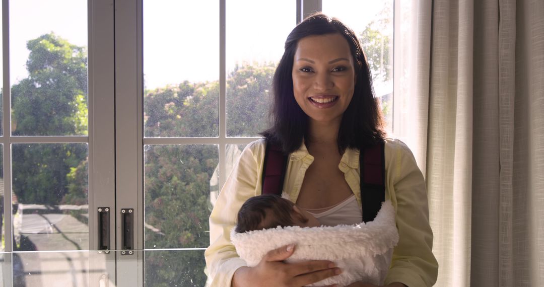 Mother Using Baby Carrier Near Sunny Window at Home