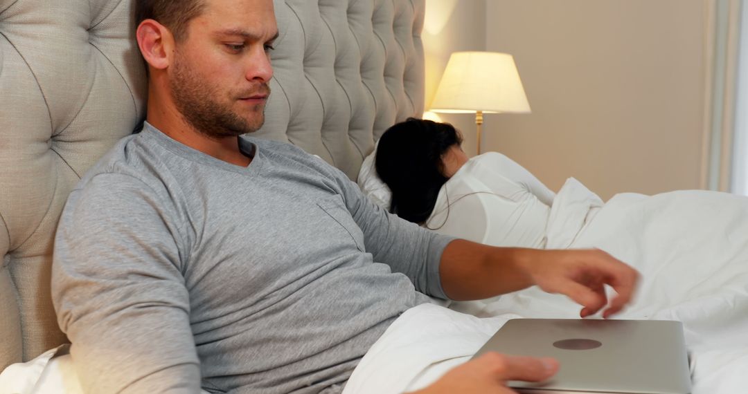 Man Using Laptop in Bed While Woman Sleeping - Free Images, Stock Photos and Pictures on Pikwizard.com