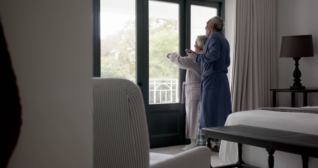 Elderly Couple in Robes Enjoying Morning View from Bedroom Window - Free Images, Stock Photos and Pictures on Pikwizard.com