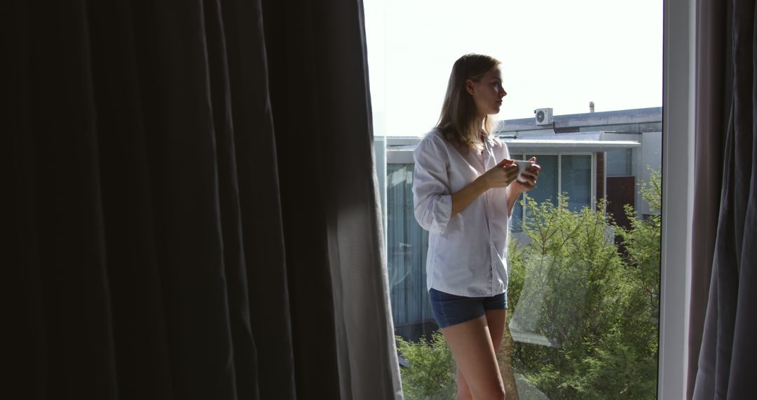 Young Woman Drinking Coffee by Sunny Window in Casual Clothing - Free Images, Stock Photos and Pictures on Pikwizard.com