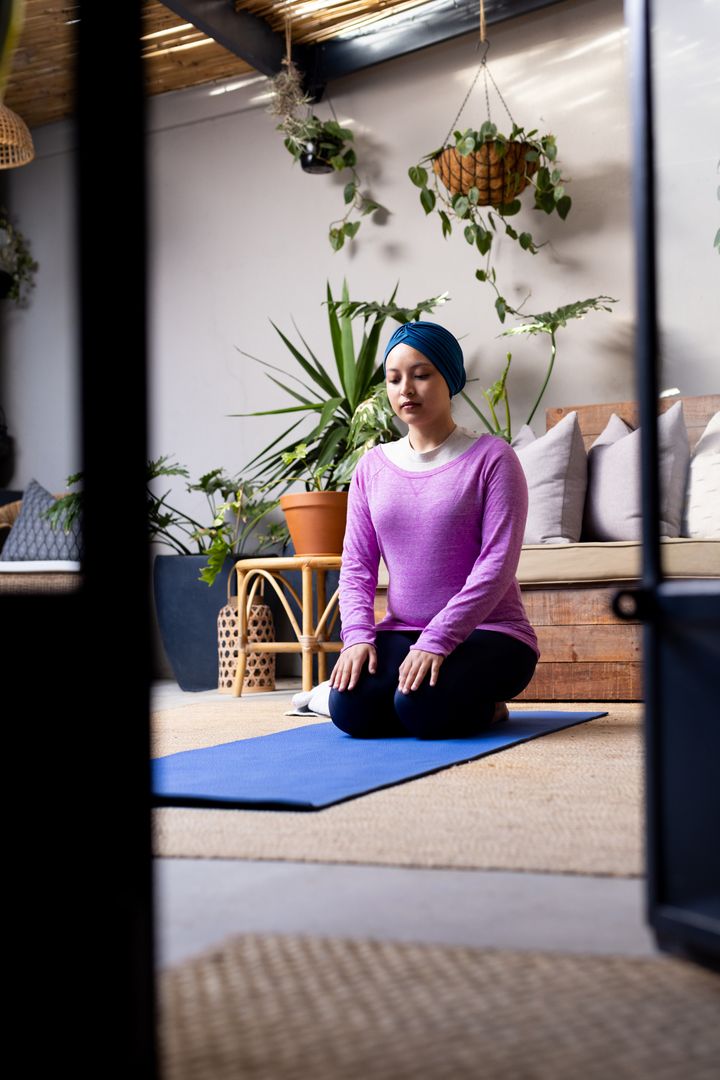 Vertical image of relaxed biracial woman in hijab in yoga pose kneeling in living room, copy space - Free Images, Stock Photos and Pictures on Pikwizard.com