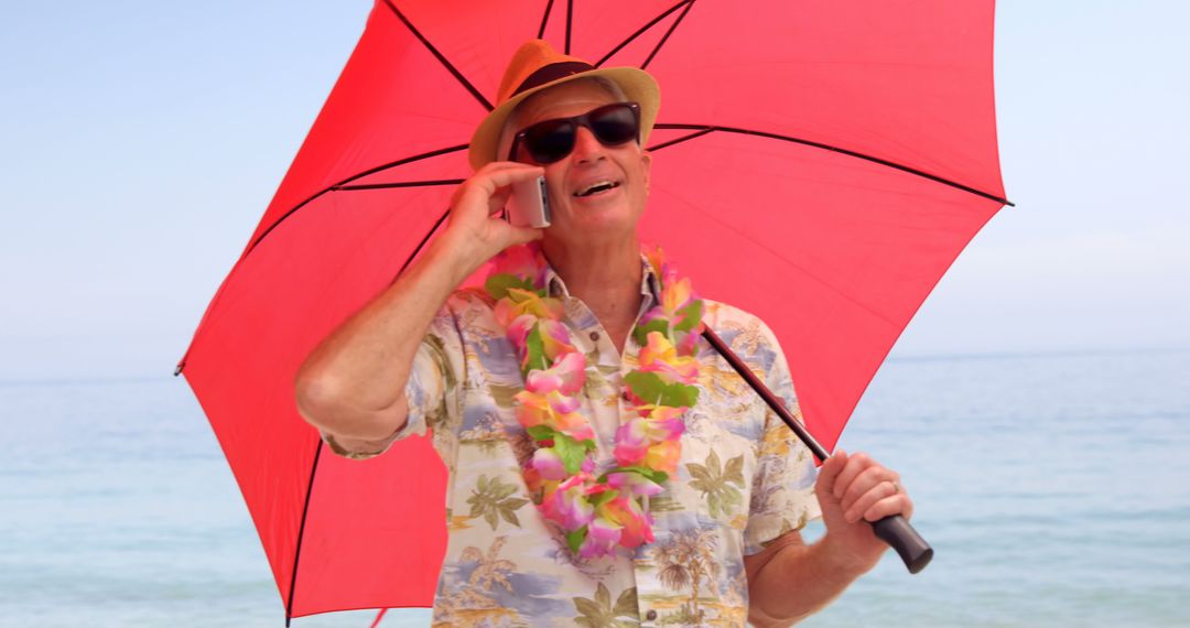 Smiling Elderly Man in Hawaiian Shirt Chatting on Phone, Holding Red Umbrella at Beach - Free Images, Stock Photos and Pictures on Pikwizard.com