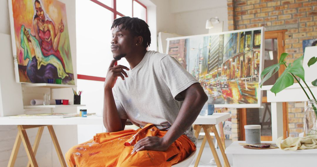 Thoughtful Artist Sitting in Studio Surrounded by Colorful Paintings - Free Images, Stock Photos and Pictures on Pikwizard.com