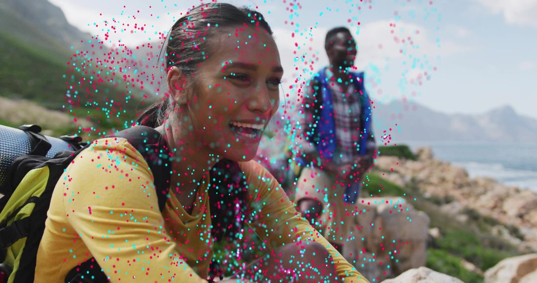 Smiling hiker sitting on coastal mountain trail overlooking ocean with companion and backpacks