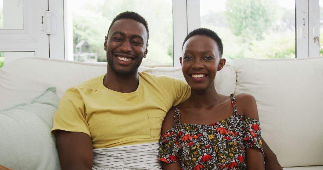 Portrait of happy african american couple sitting on sofa embracing and smiling to camera - Free Images, Stock Photos and Pictures on Pikwizard.com