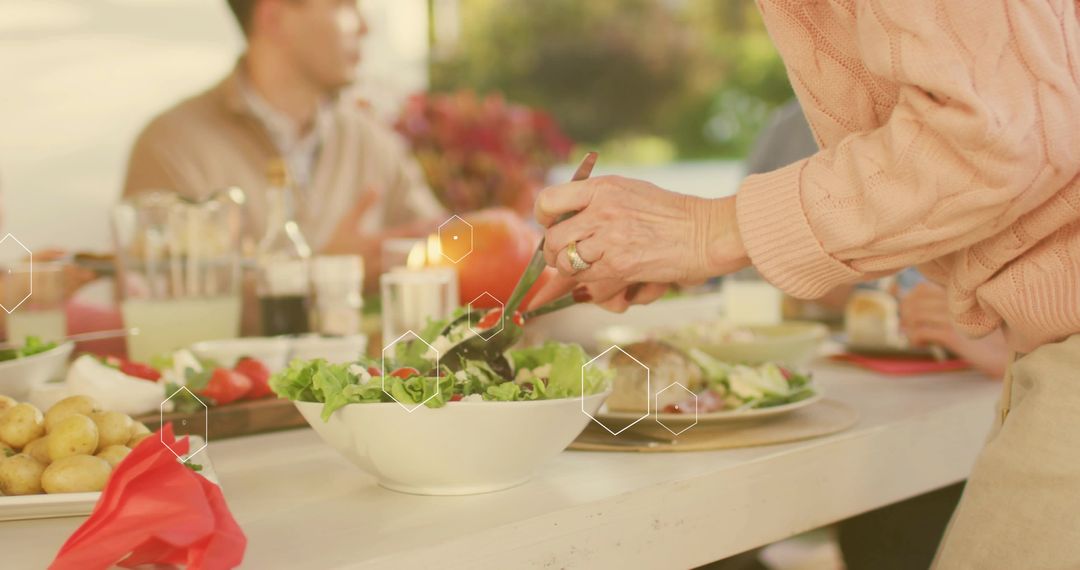 Tossing salad at sunlit outdoor gathering with pink sweater, rustic table and candlelight