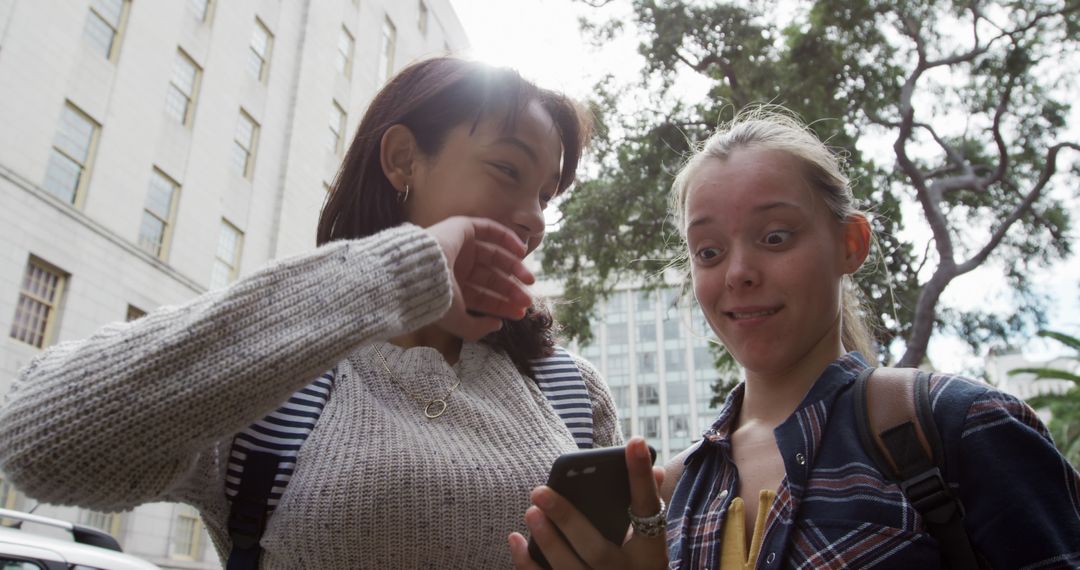 Two Excited Students Looking at Smartphone in Urban Setting - Free Images, Stock Photos and Pictures on Pikwizard.com