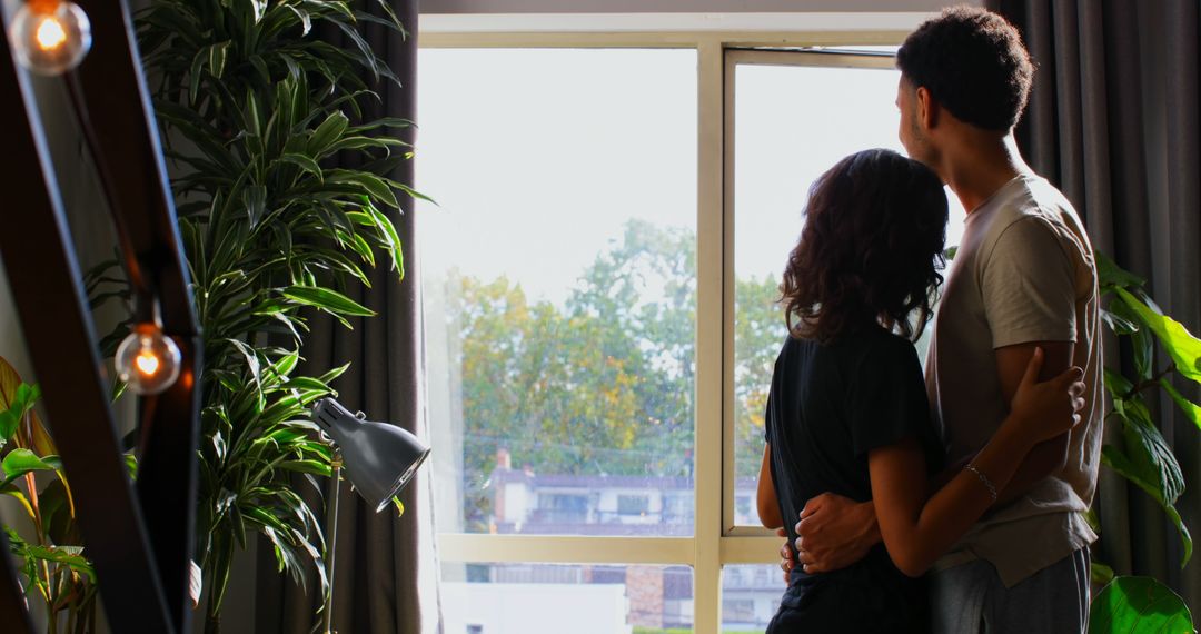 Couple Embracing and Looking Out Window in Cozy Apartment - Free Images, Stock Photos and Pictures on Pikwizard.com