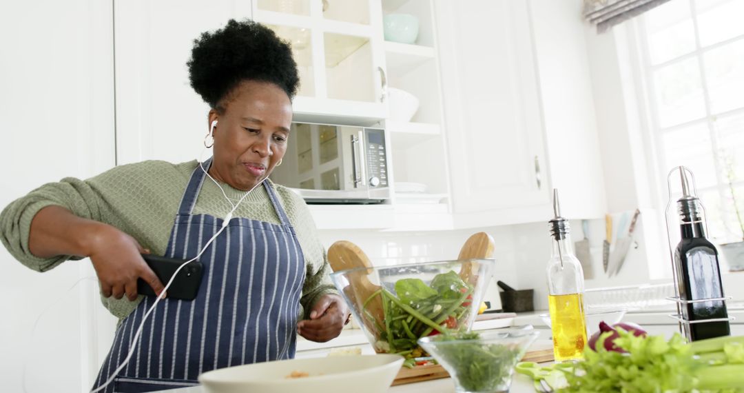 Woman in apron listening to music while preparing healthy salad in modern kitchen - Free Images, Stock Photos and Pictures on Pikwizard.com