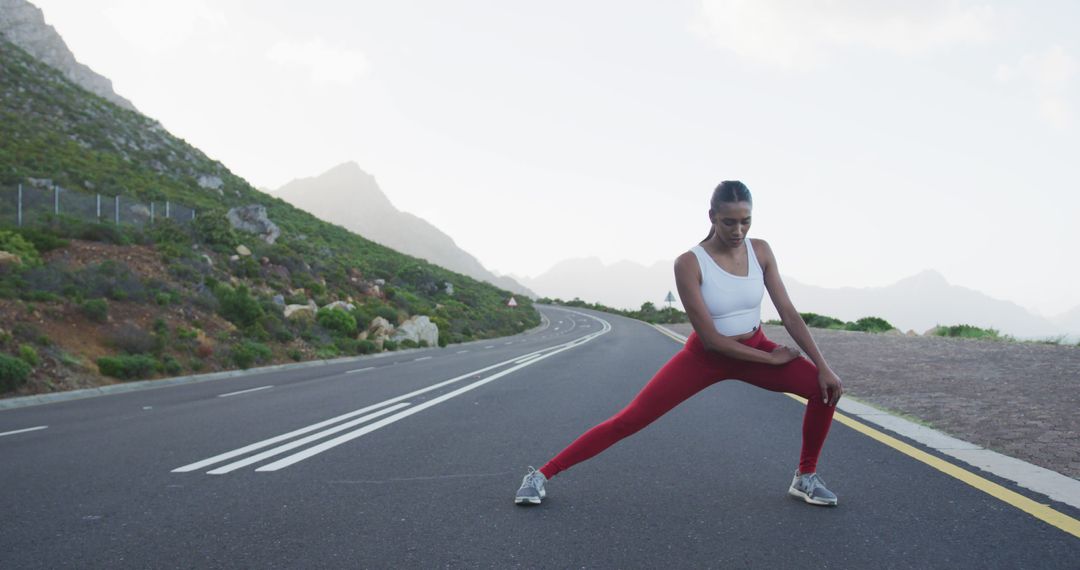 Woman stretching on open road in mountains with white sports top and red leggings - Free Images, Stock Photos and Pictures on Pikwizard.com